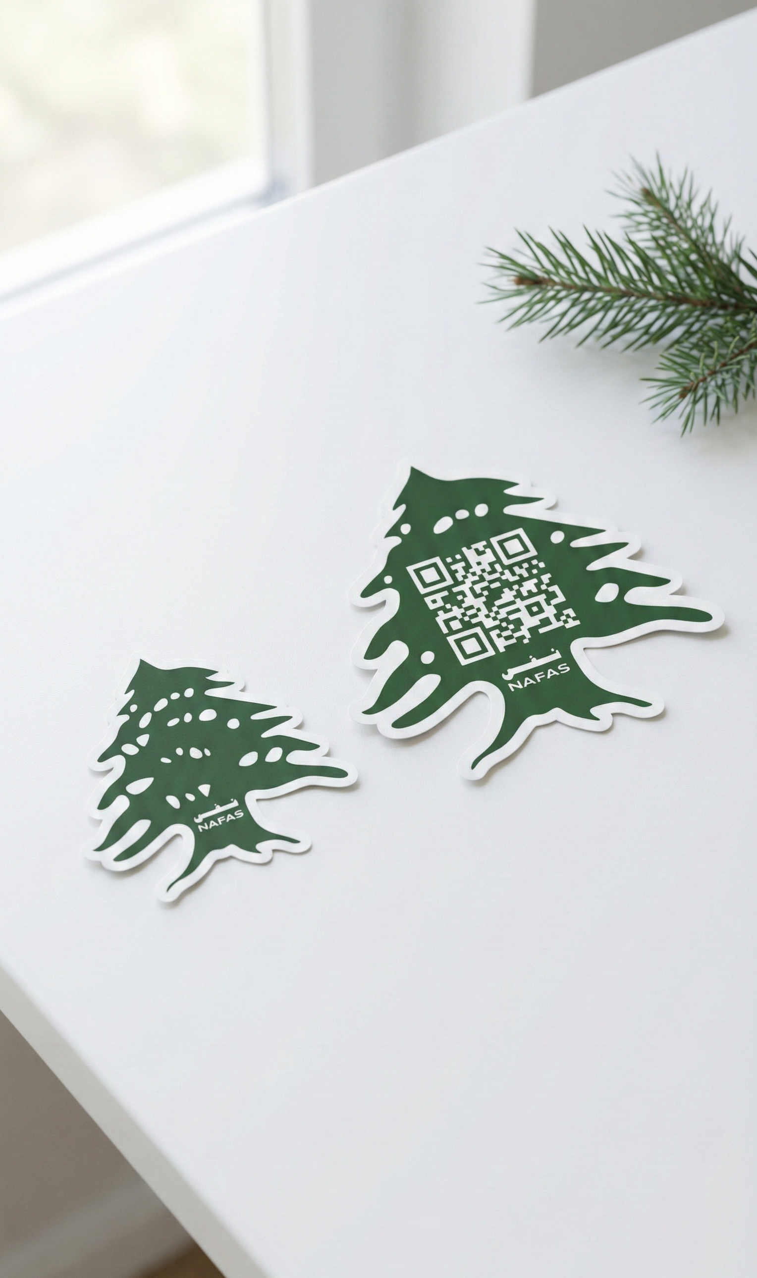 Two green Lebanese cedar-shaped Nafas stickers on a white desk, one with a scannable QR code, minimal clean lifestyle photo.