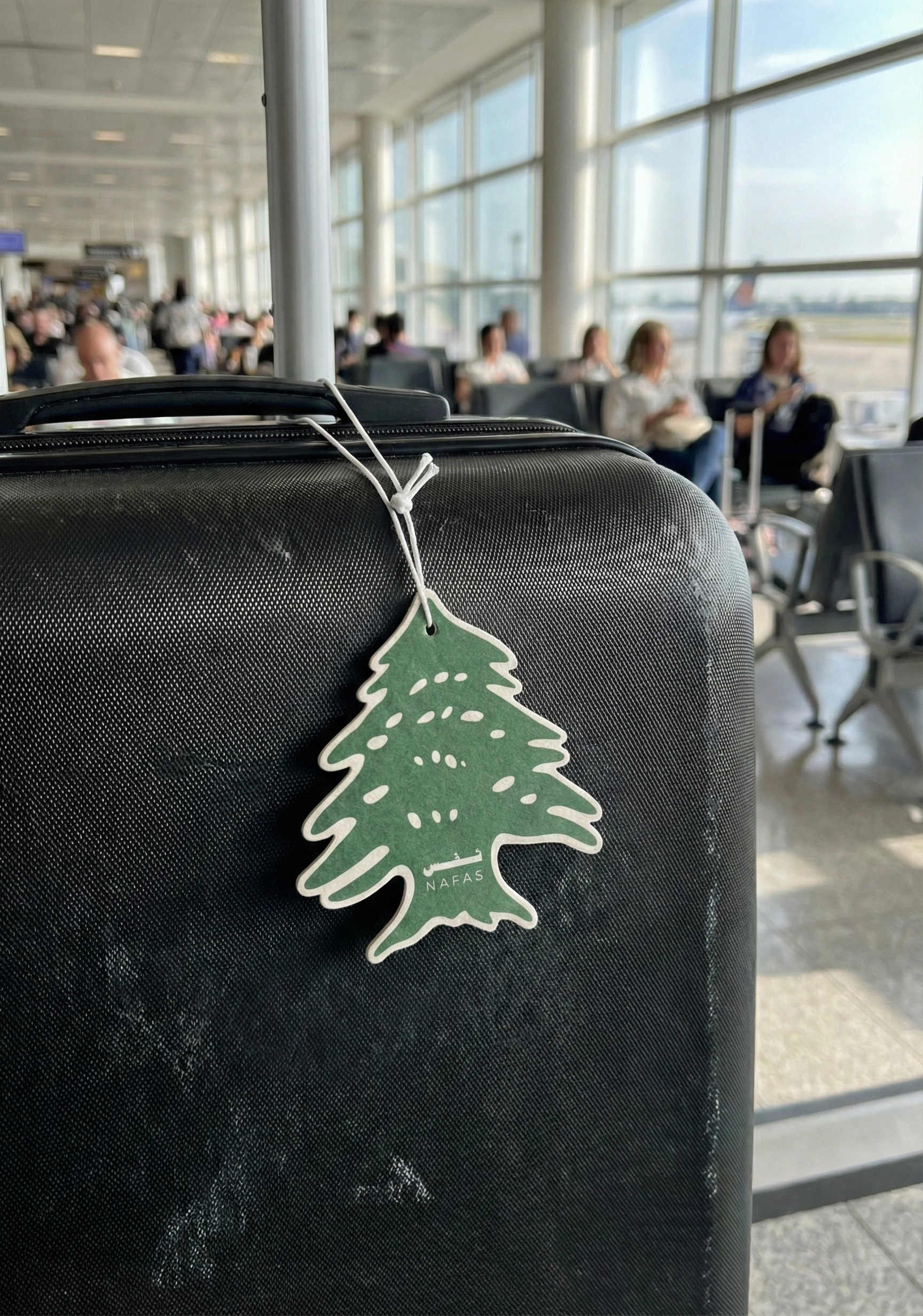 Nafas Lebanese cedar air freshener hanging from a suitcase handle in an airport terminal