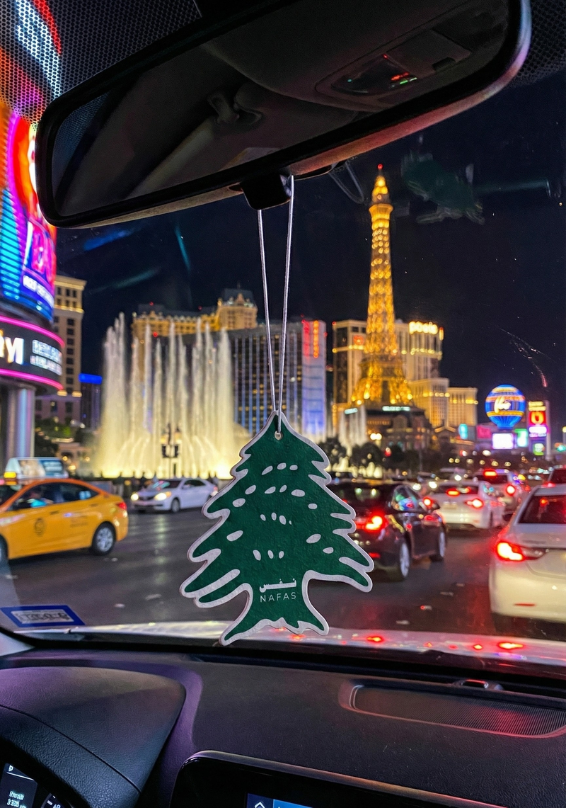 Las Vegas Strip at night seen from inside a car with Bellagio fountains and the Paris Las Vegas Eiffel Tower, plus a Nafas Lebanese cedar air freshener hanging from the rearview mirror