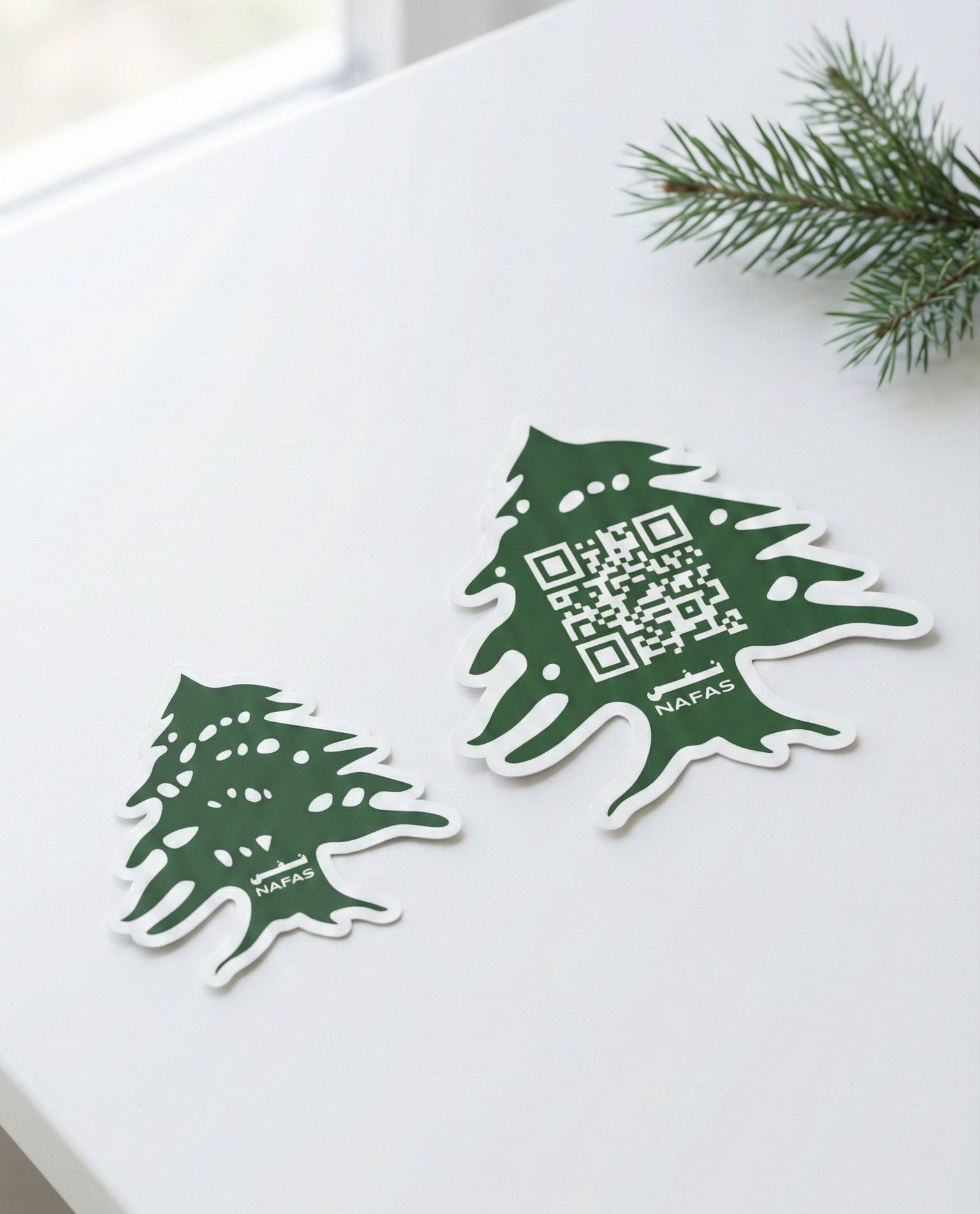 Nafas Lebanese cedar sticker pack on a white table—one QR code cedar sticker and one Nafas logo cedar sticker, with pine branch detail.